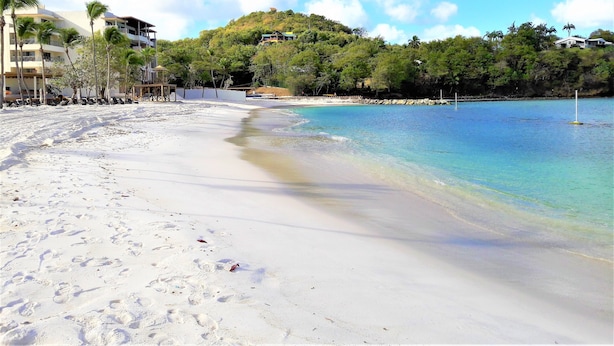 Uma praia com águas turquesa cristalinas, areia branca e colinas verdejantes ao fundo.
