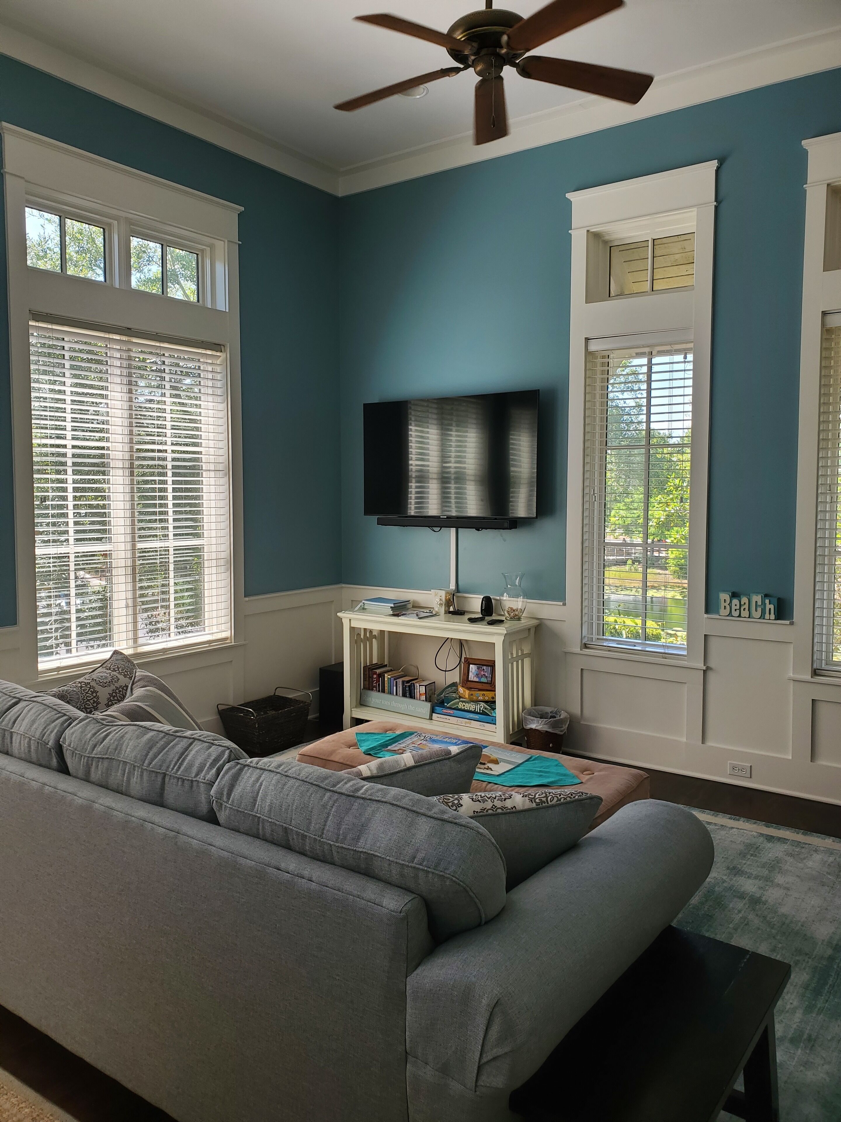 Un salón con un sofá gris, un televisor montado en la pared y una pequeña mesa con libros y objetos decorativos.