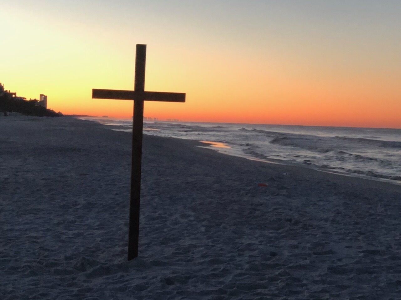 A wooden cross on a beach at sunset.