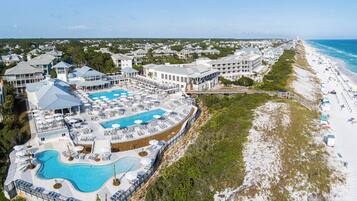 An aerial view of a resort with a large pool, beach, and multiple buildings.