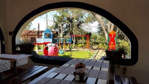 A view through a window of a restaurant with a patio area, featuring outdoor play equipment and a garden. - Hotel La Quinta (Paraguari)