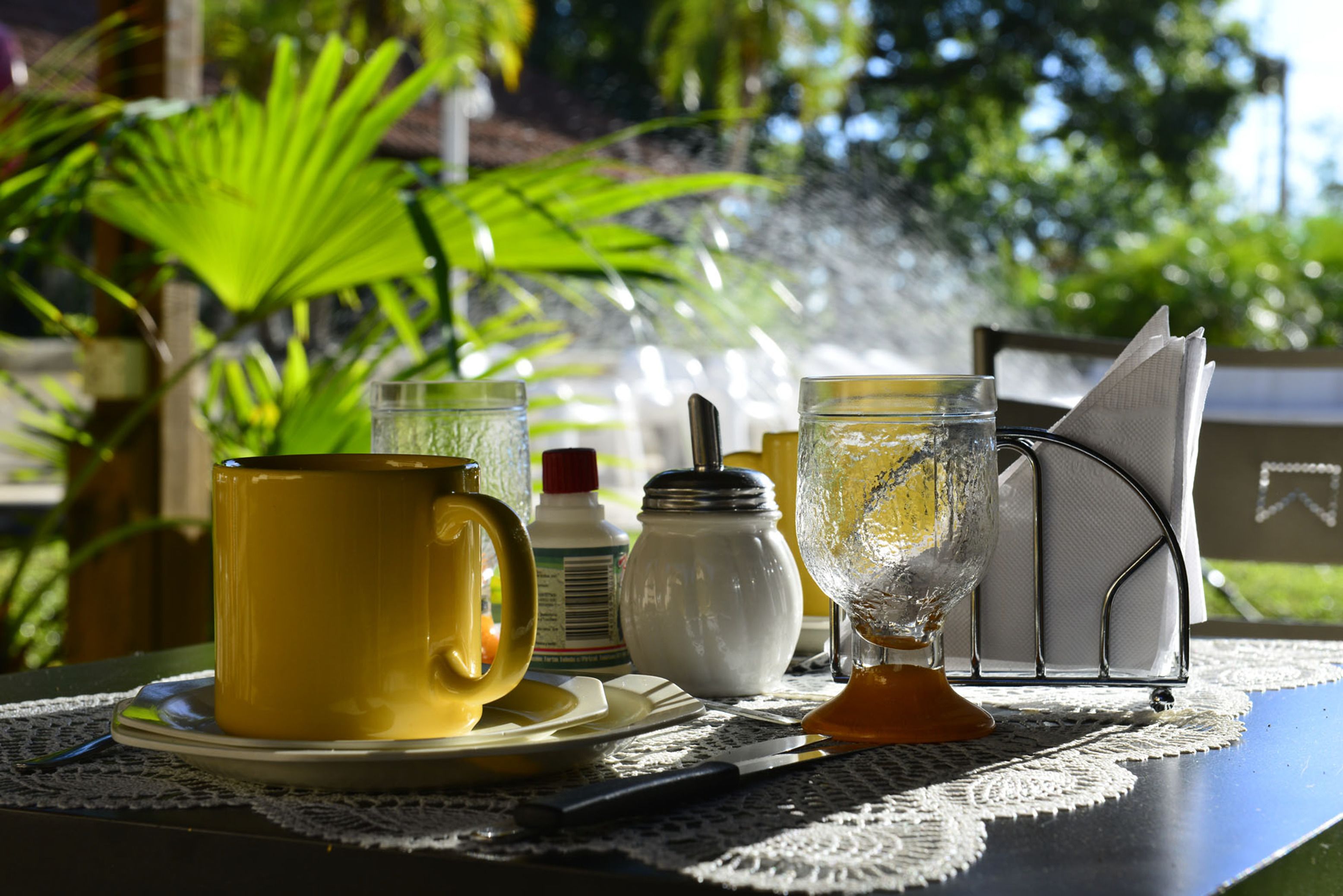 A table with a yellow mug, a glass, a bottle, and a napkin holder.