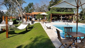 A pool area with a wooden deck, lounge chairs, and a gazebo. - Hotel La Quinta (Paraguari)
