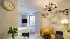 Una habitación con una cama, una mesa de comedor con sillas, un sillón amarillo, un sofá, una araña y un reloj de pared.
