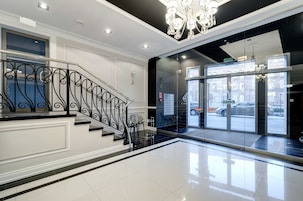 A modern hotel lobby with a staircase, a chandelier, and a view of the street through large glass doors.