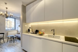 A modern kitchen with a white countertop, a sink, and a fruit bowl. There is a window with a view of buildings outside.