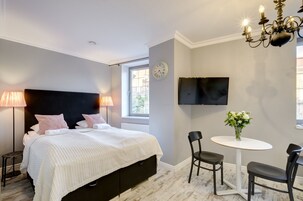 A bedroom with a bed, bedside lamps, a TV, a small table with chairs, and a window.
