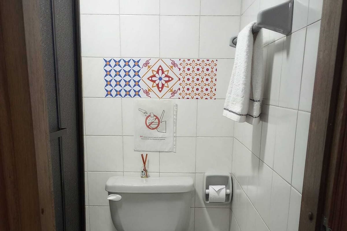 Une petite salle de bain propre, avec des toilettes, une poubelle verte et une serviette suspendue à un porte-serviettes.