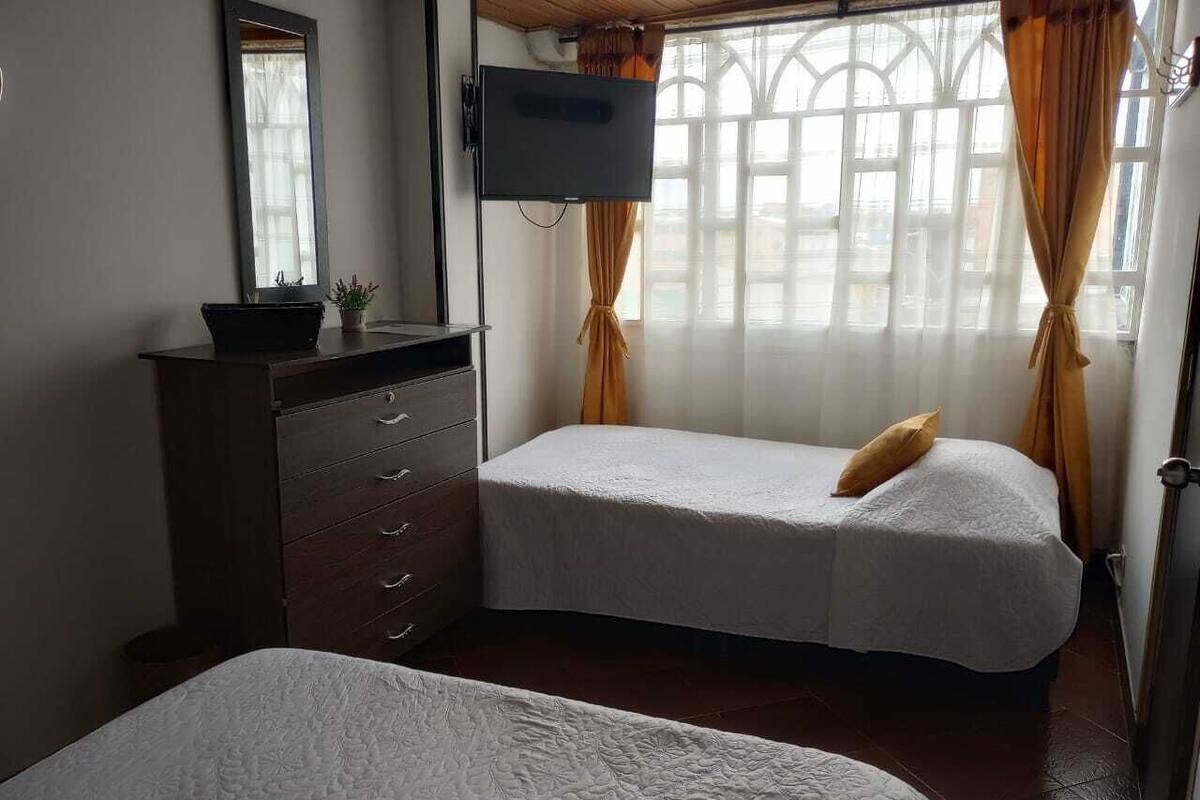 Une chambre avec deux lits, une commode, une télévision et une fenêtre avec des rideaux.