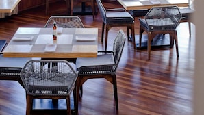 Un restaurant avec des tables et des chaises en bois, de grandes fenêtres donnant sur un paysage verdoyant, et des parasols rouges et verts suspendus.