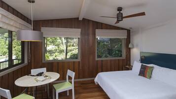 A bedroom with a bed, a ceiling fan, a table with chairs, and large windows with curtains.