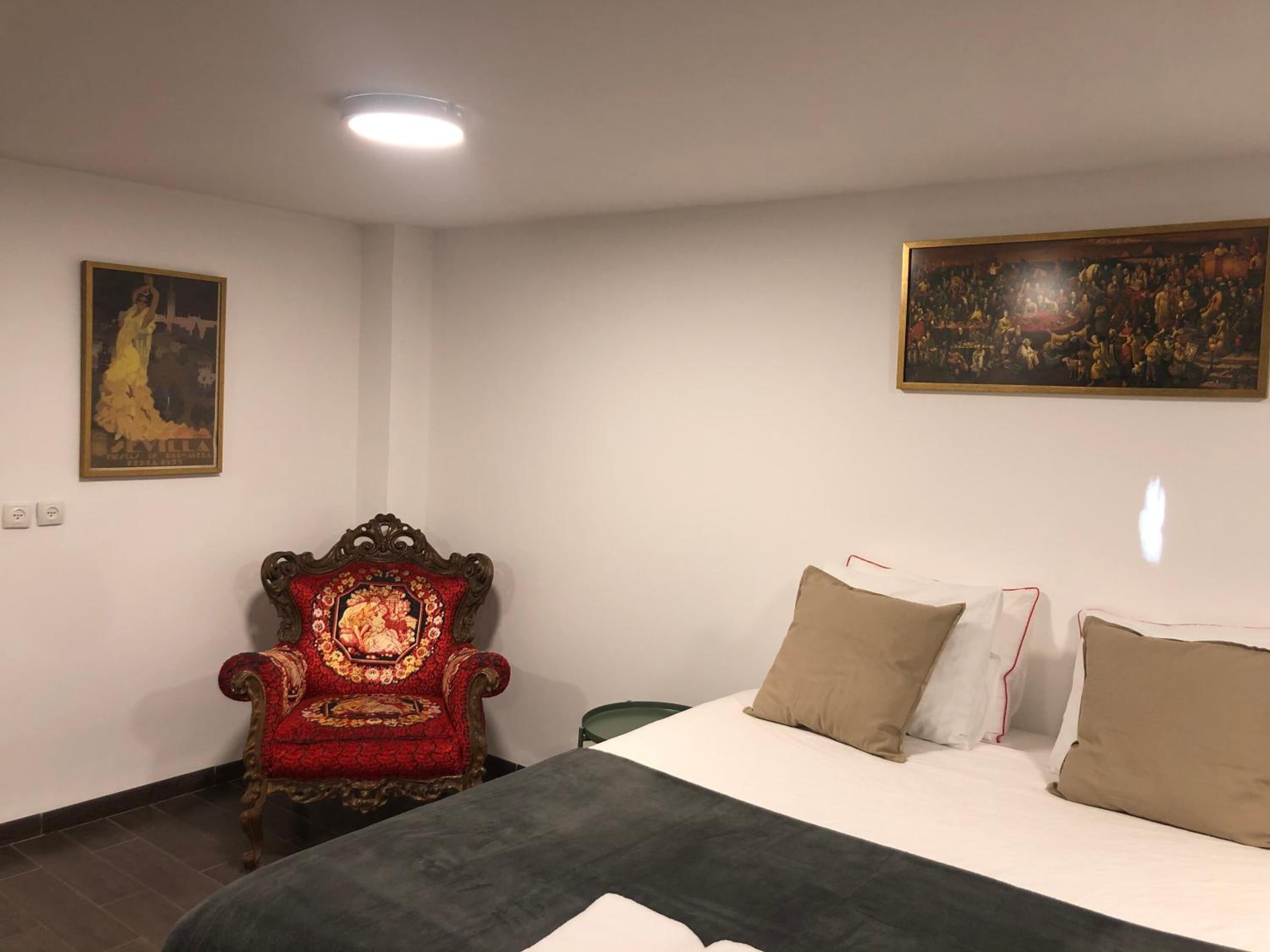 A bedroom with a bed, a chair, and two paintings on the walls.