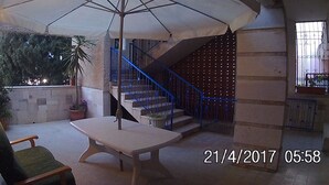 An outdoor patio area with a table and chairs, a large umbrella, a staircase, and a potted plant. - Hassan guest house (Nazareth)