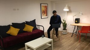 A living room with a red sofa, a white coffee table, a desk with a computer, a lamp, and a speaker. - Hassan guest house (Nazareth)