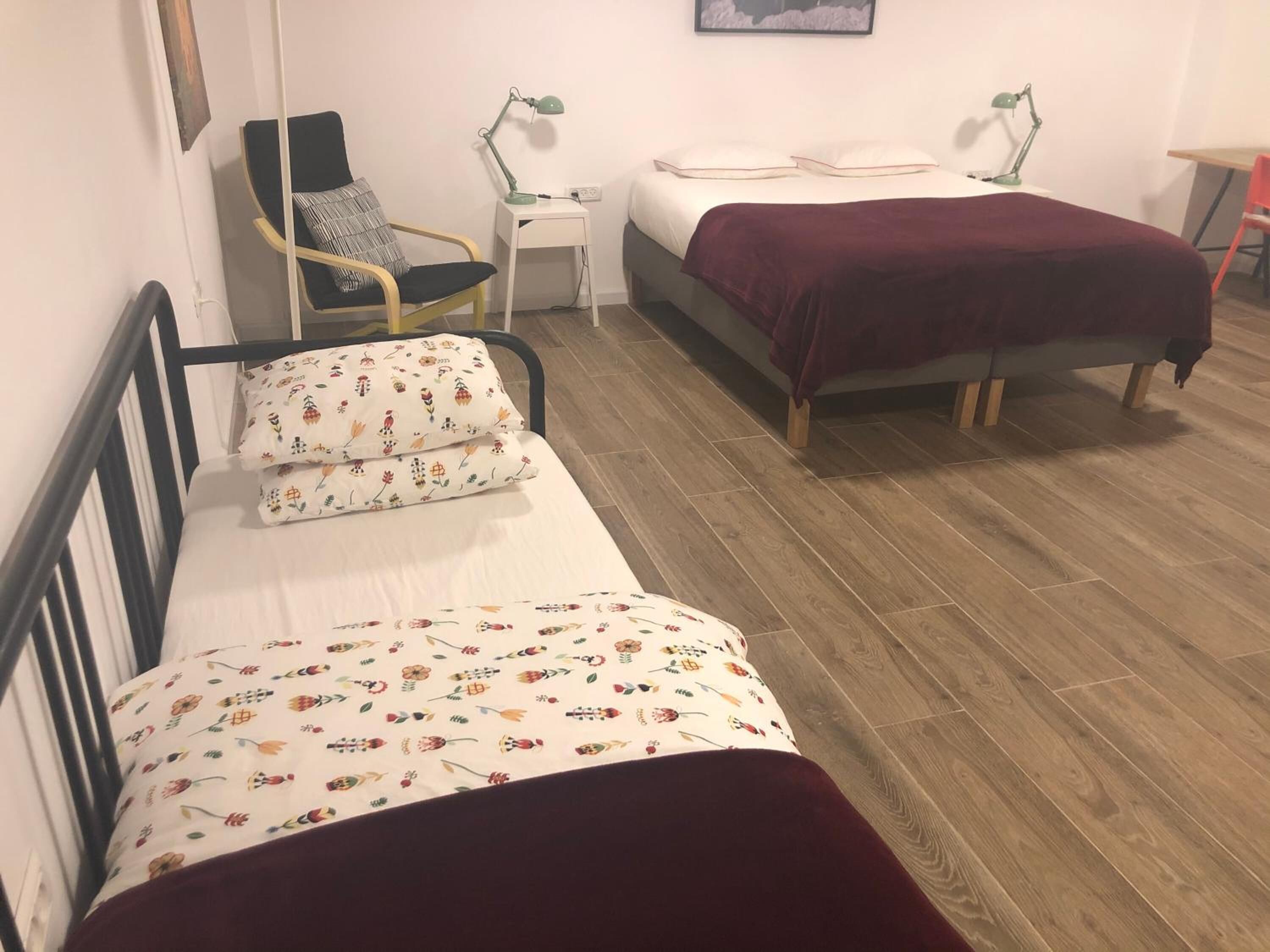 Ein Zimmer mit einem Bett, einem Sessel, einem kleinen Tisch und einem Schreibtisch.