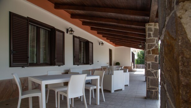 Un patio al aire libre con mobiliario blanco, pilares de piedra y vigas de madera.