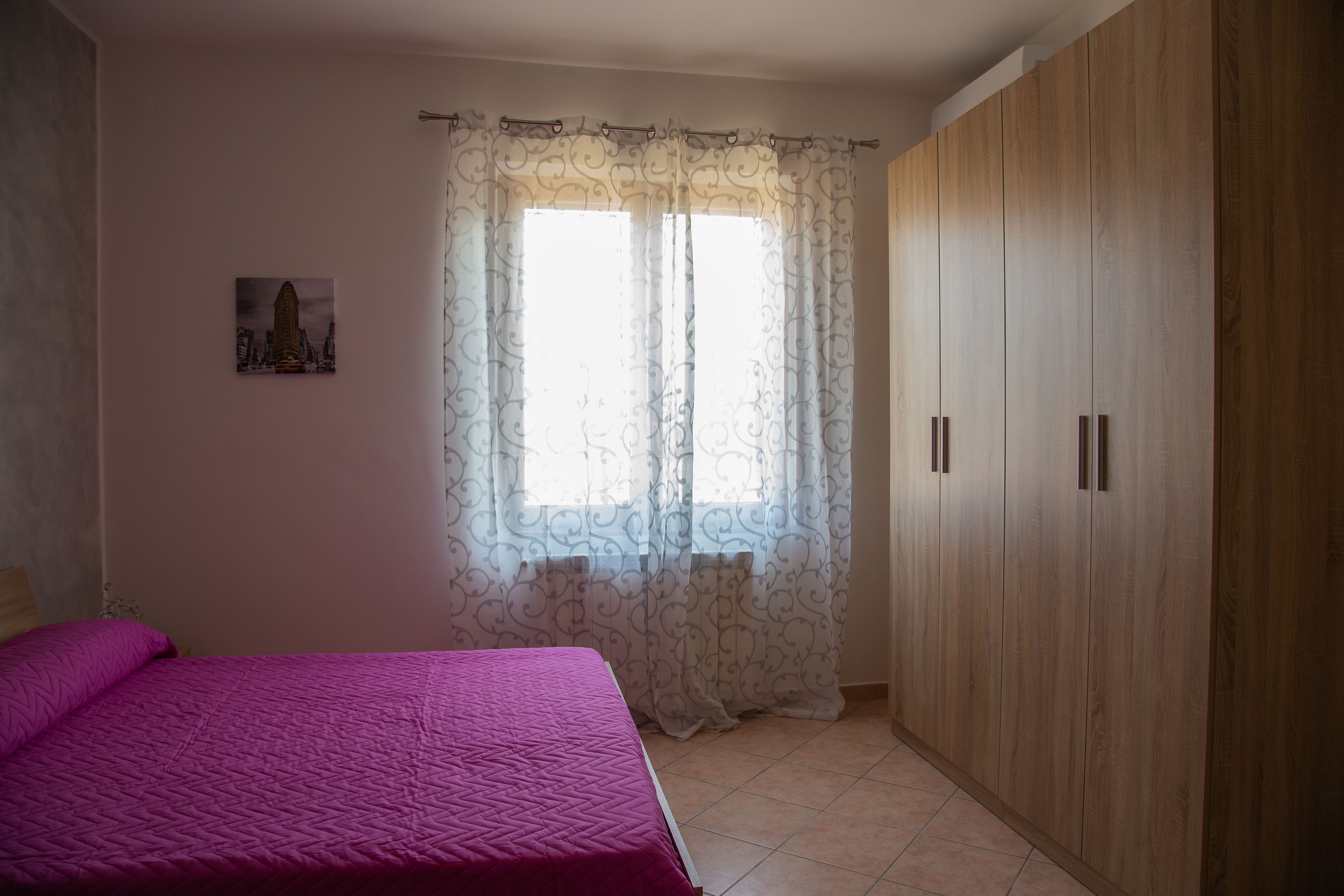 Un dormitorio con cama, armario y ventana con cortinas.