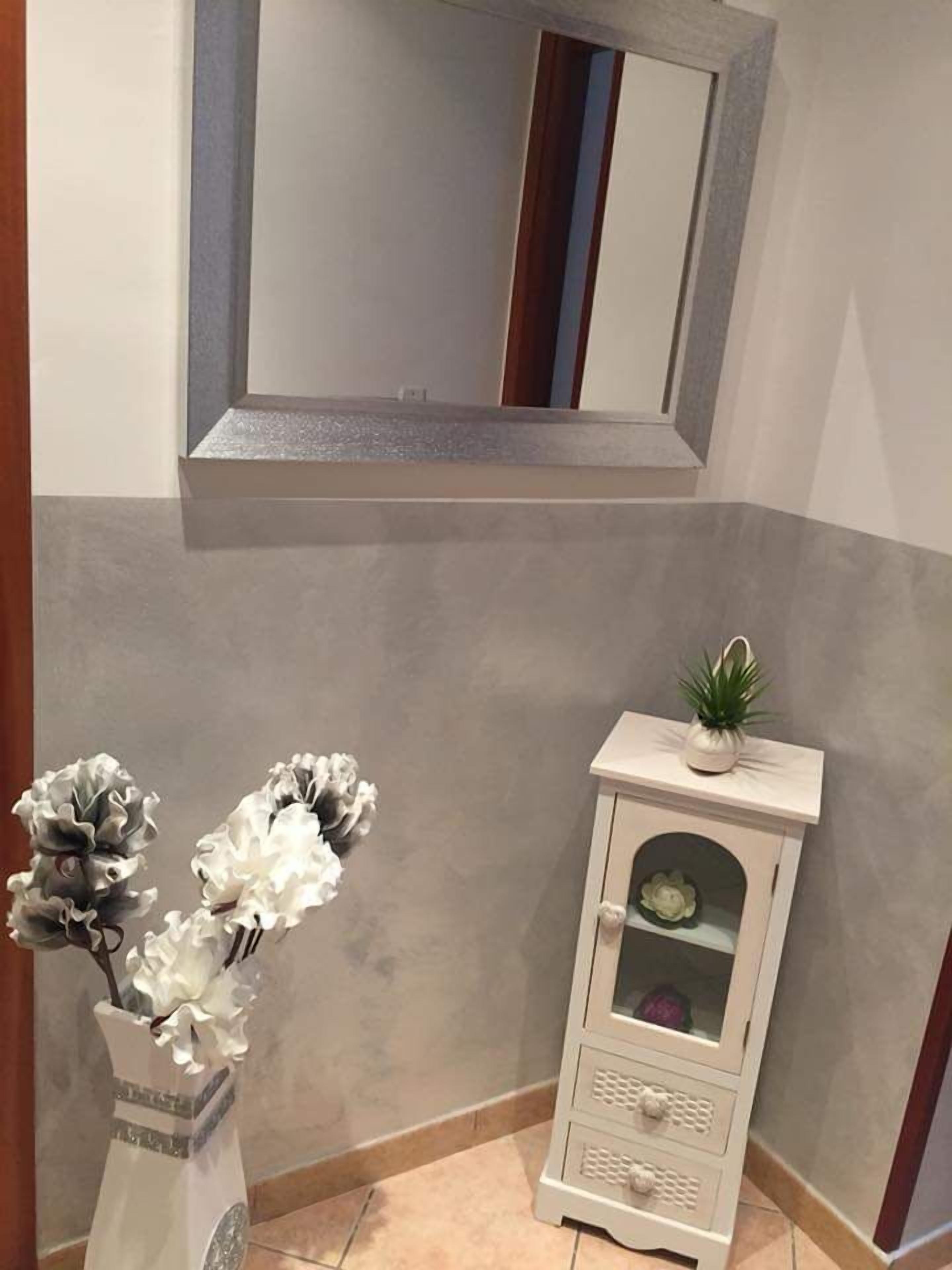 A corner of a room with a white console table, a vase with white flowers, and a mirror above.