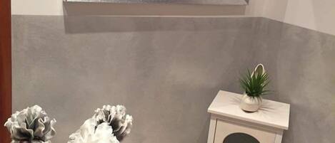 A corner of a room with a white console table, a vase with white flowers, and a mirror above.