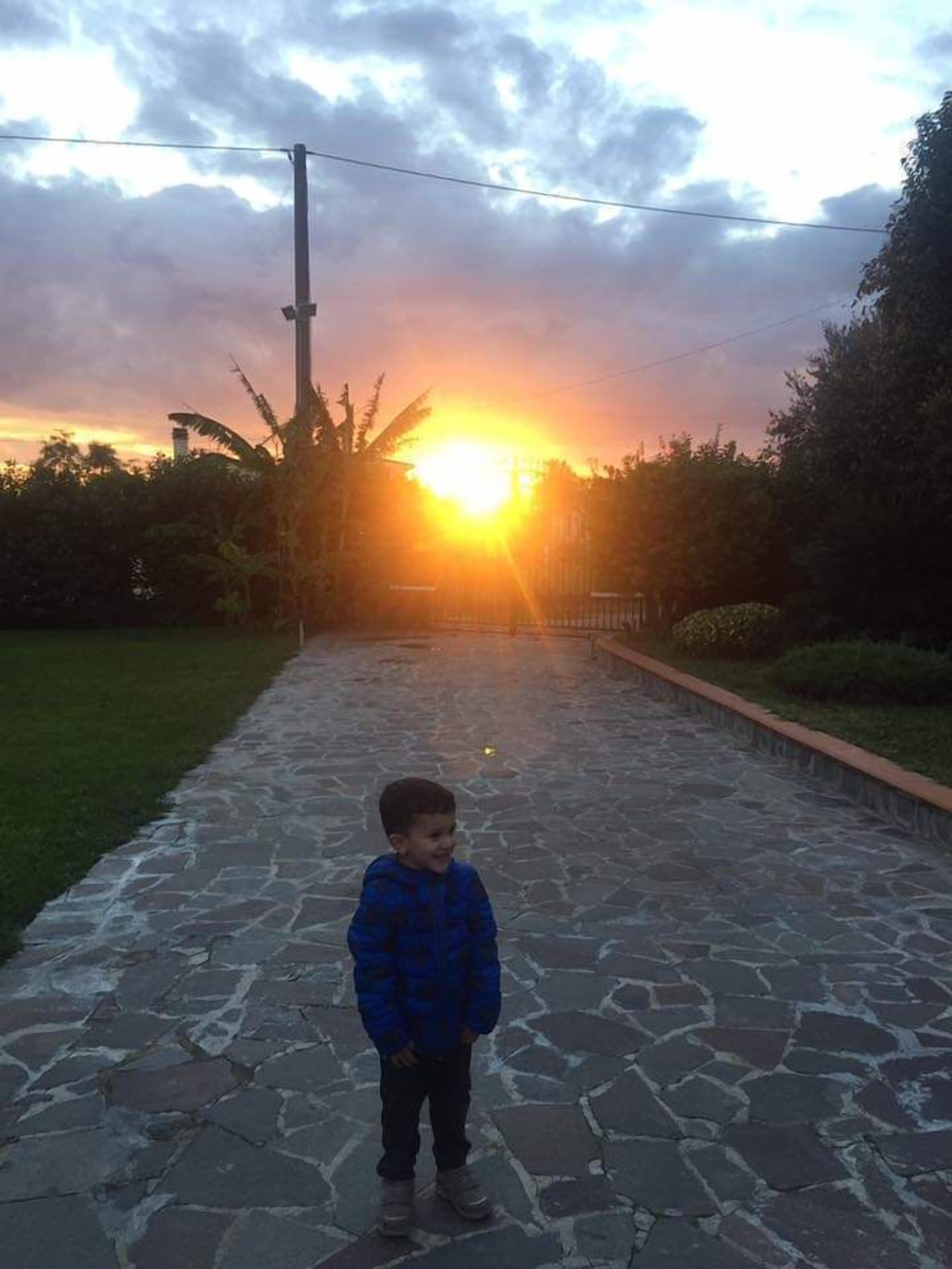Un bambino in piedi su un sentiero di pietra con un tramonto sullo sfondo.