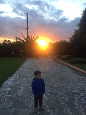 Un niño de pie sobre un sendero de piedra con un atardecer de fondo.