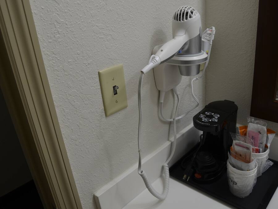 A hairdryer mounted on a wall, a coffee maker, and a tray with toiletries.