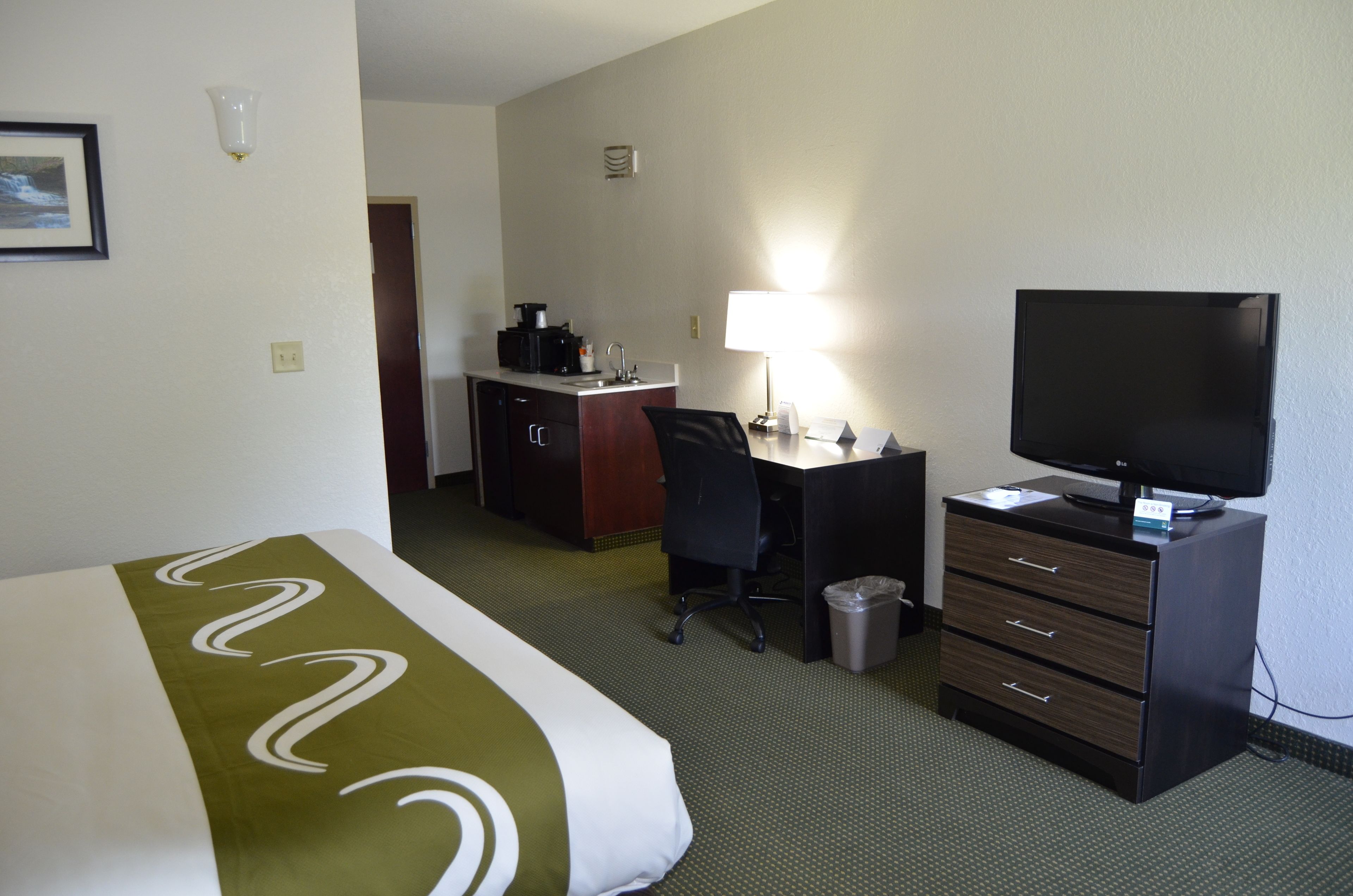 A hotel room with a bed, a desk, a chair, a television, and a trash can.