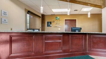 A reception desk with a wooden panel design, a sign for 'Quality Inn', and a check-in/out schedule on the wall.
