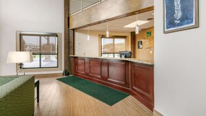 A hotel reception area with a counter, a window, a green rug, and a framed artwork on the wall.