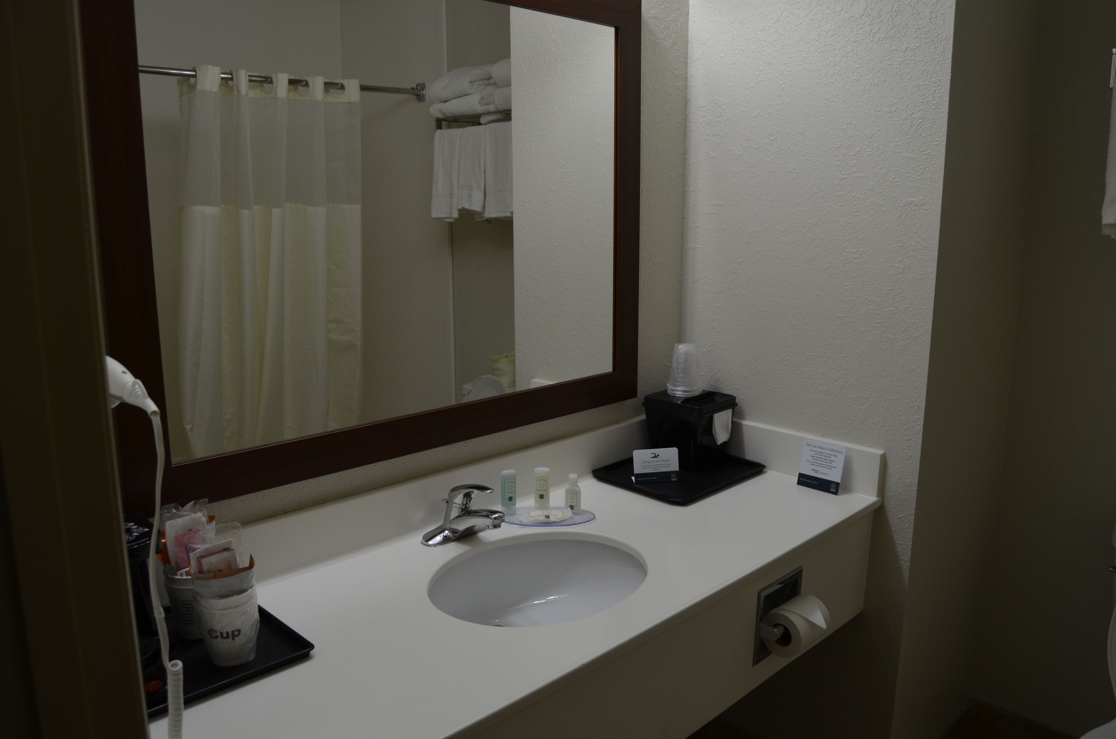 Une salle de bain d’hôtel avec un lavabo blanc, un miroir, un porte-serviettes avec des serviettes pliées et une machine à café.