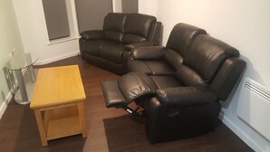 Ein Wohnzimmer mit zwei schwarzen Ledersofas, einem Holztisch als Couchtisch und einem Glastisch.