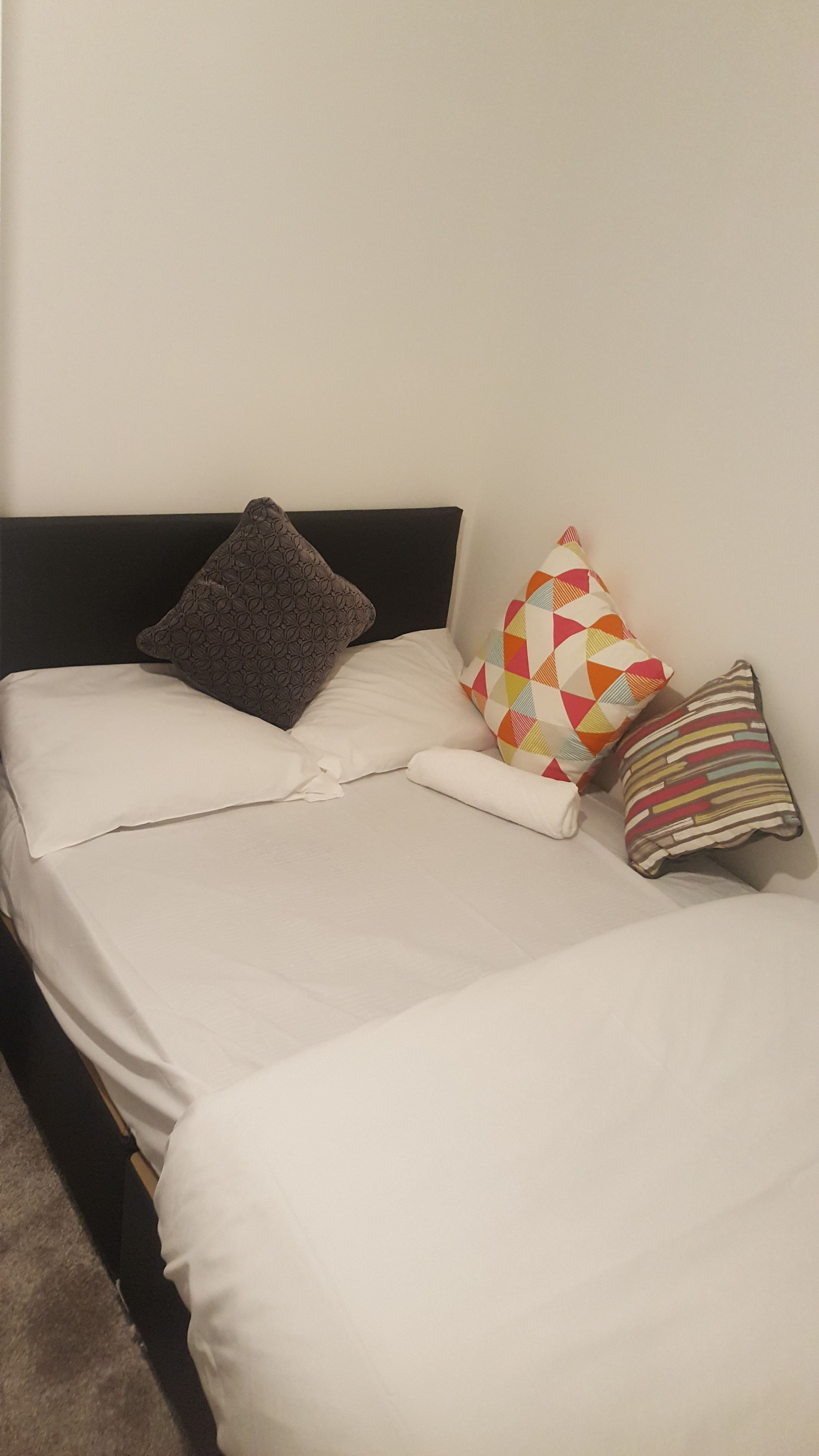 A bed with white bedding and three pillows of different patterns.