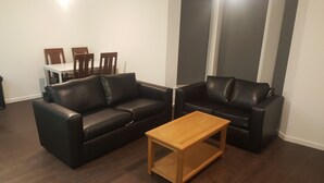 Ein Wohnzimmer mit zwei schwarzen Ledersofas, einem Holztisch und einem Essbereich mit einem weißen Tisch und Holzstühlen.