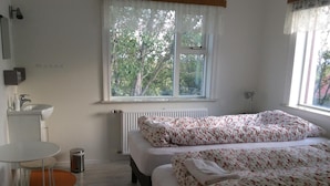 Ein Schlafzimmer mit zwei Betten, einem Fenster mit Blick auf Bäume, einem Heizkörper, einem Waschbecken und einem kleinen Tisch.