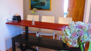 Ein Essbereich mit Holztisch, weißen Stühlen, einer Blumenvase und einer Bank.