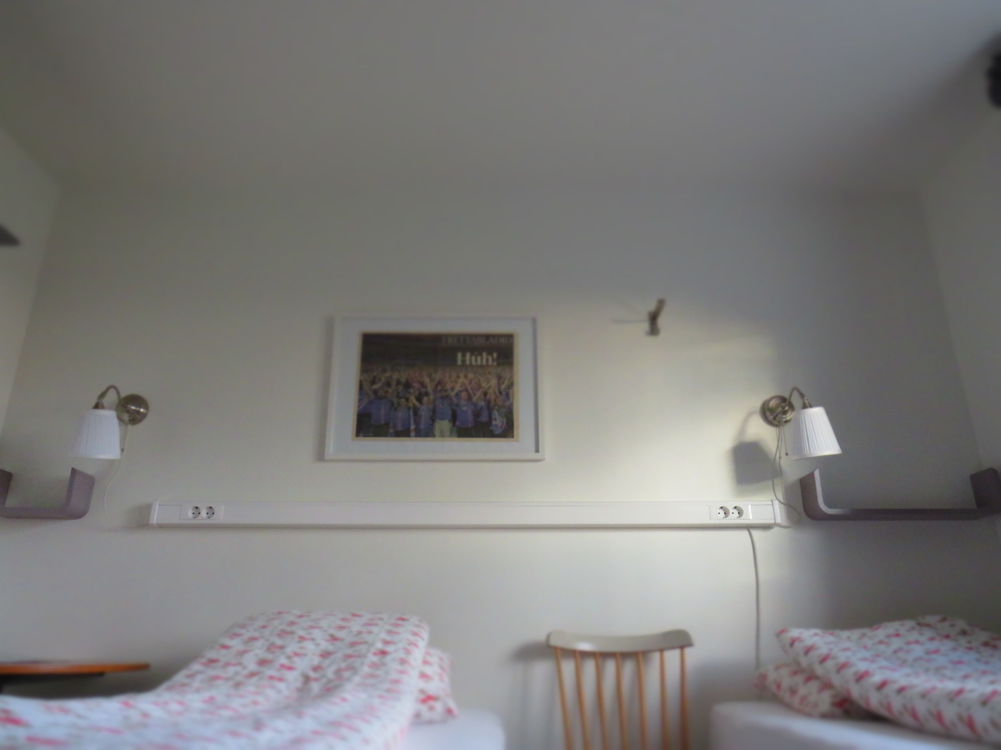 Un dormitorio con dos camas, una estantería en la pared con un cuadro enmarcado y lámparas de noche.