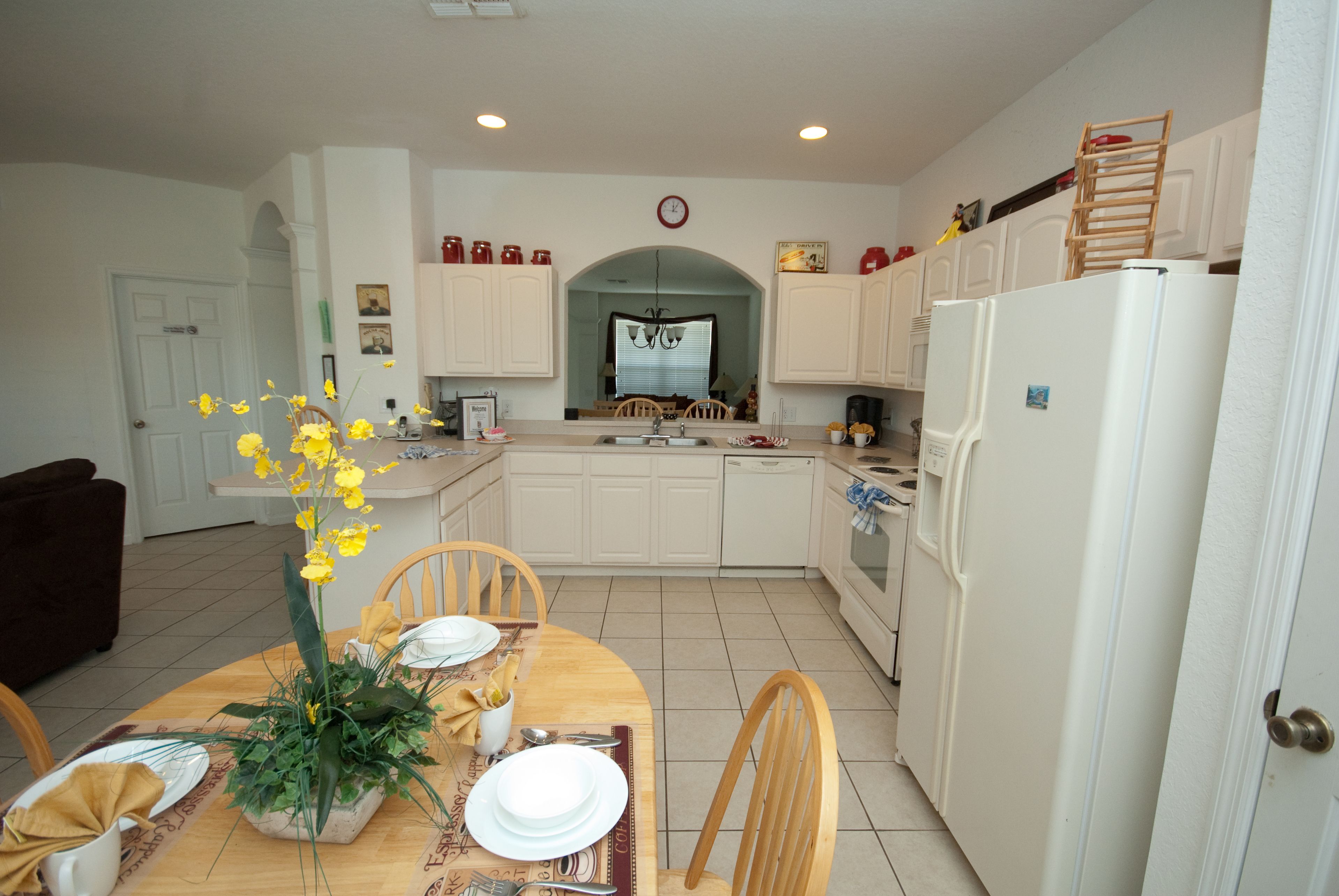 A modern kitchen with white cabinets, a dining table set for four, and a refrigerator.