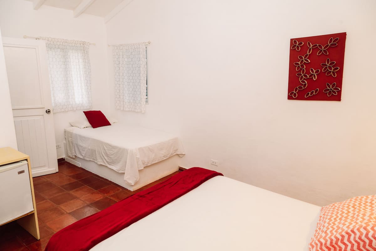 A bedroom with a bed, a small bedside table, a wardrobe, and a red artwork on the wall.