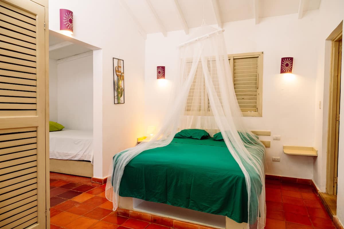 A bedroom with a bed under a canopy, a bedside table, a nightstand, and a wall-mounted light fixture.