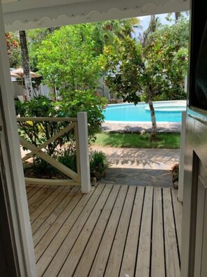 A wooden deck leading to a pool area with a view of lush greenery and a clear blue pool. - Hotel Casa Nina (Las Terrenas)