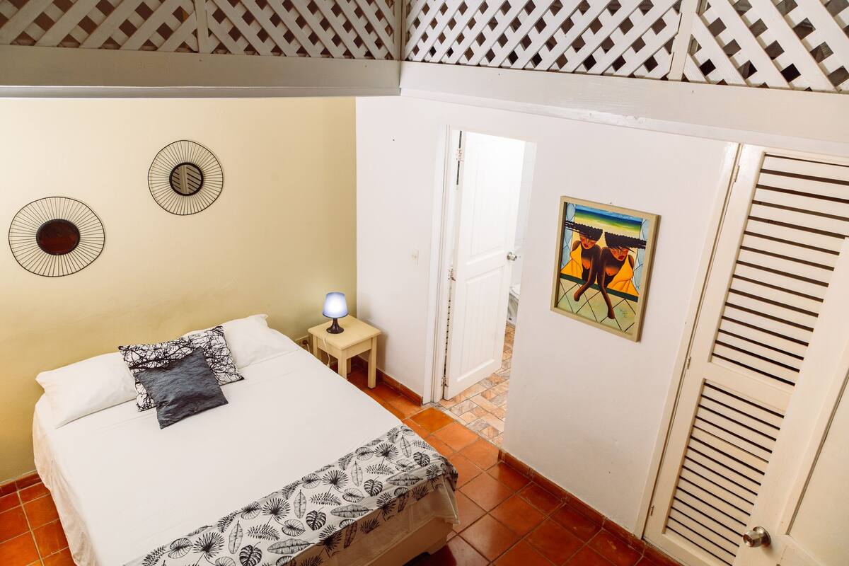 A bedroom with a bed, a nightstand with a lamp, a door, and a wall with two circular wall decorations.