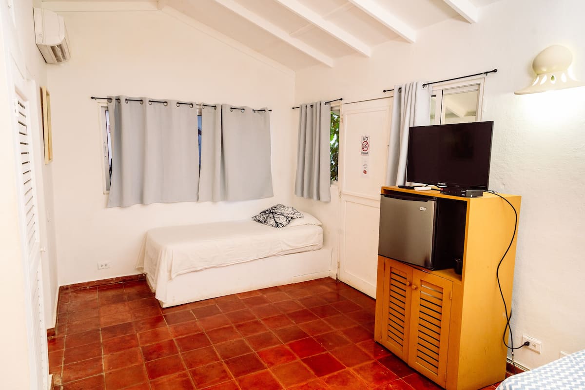 A small room with a bed, a TV on a wooden cabinet, and a window with curtains.