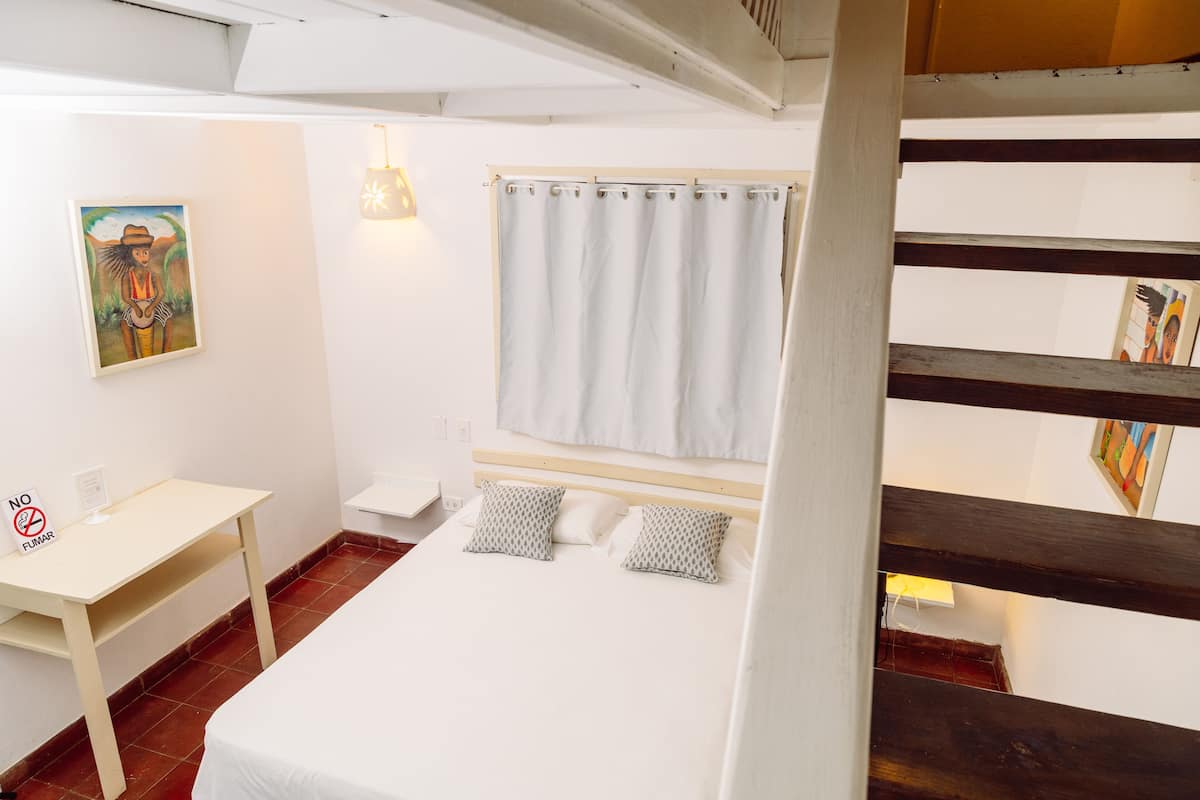 A room with a bed, a desk, a painting, and a curtain.