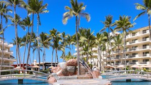 A resort pool area with palm trees, a bridge, and a building with balconies. - Villa del Palmar Beach Resort and Spa - All Inclusive (Puerto Vallarta)