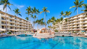 A hotel pool with palm trees, lounge chairs, and a bridge. - Villa del Palmar Beach Resort and Spa - All Inclusive (Puerto Vallarta)