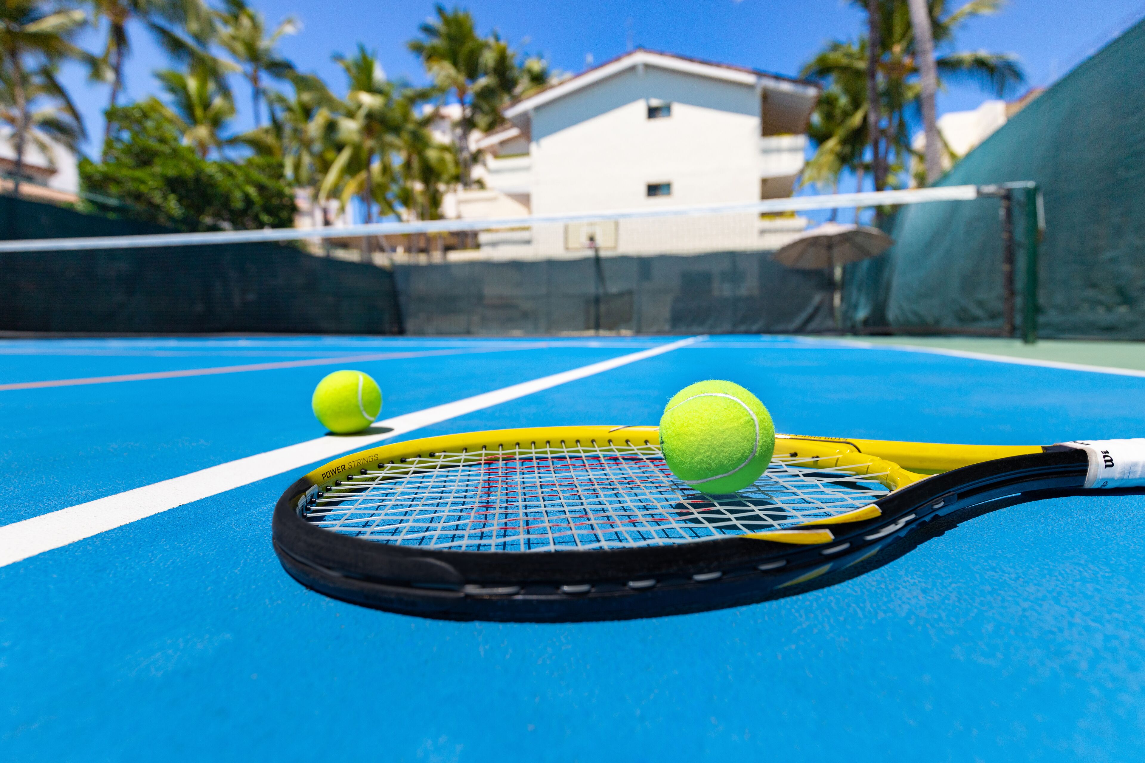 A tennis court with a net, two tennis balls, and a racket.