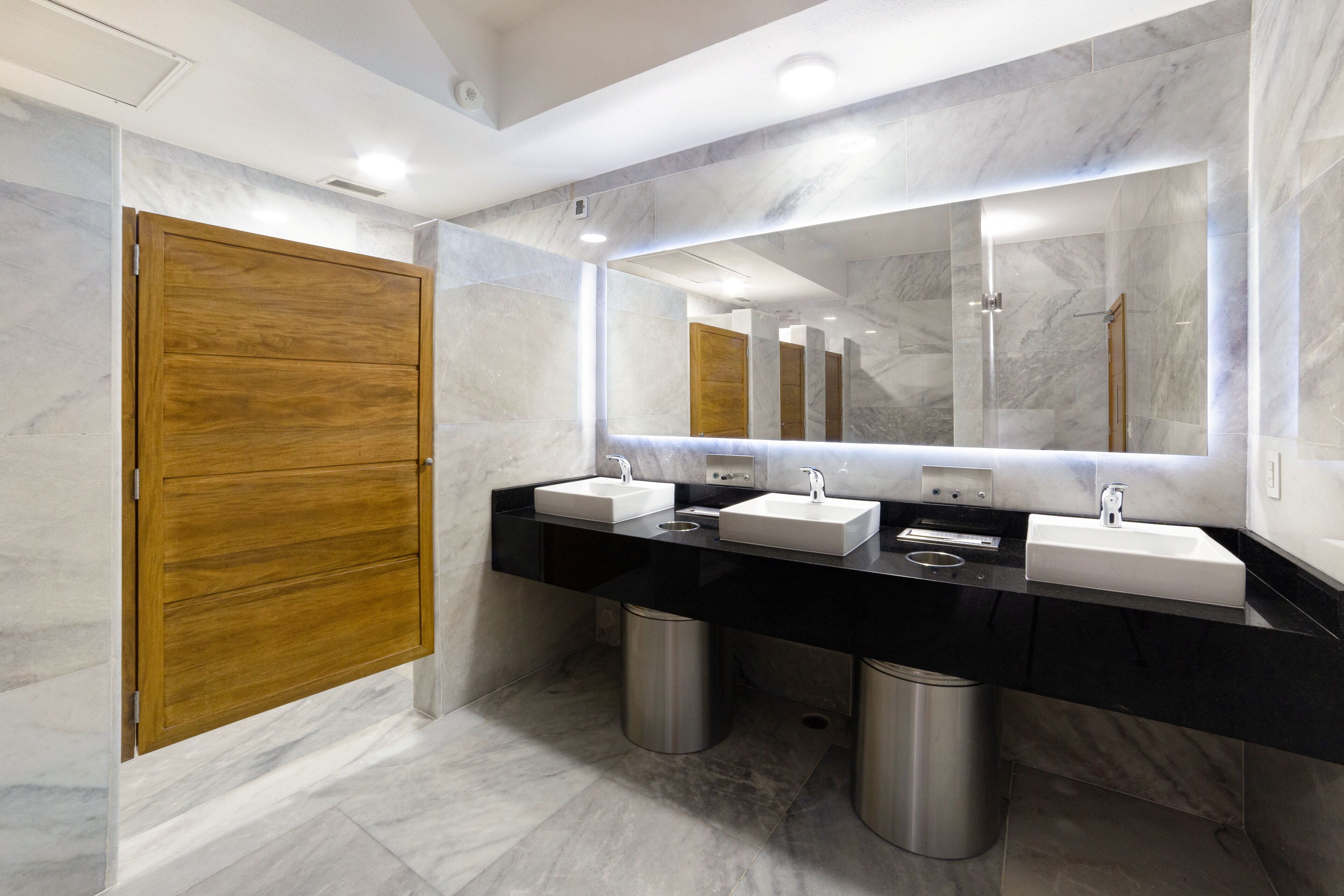 Une salle de bain moderne avec deux lavabos, un grand miroir et une porte en bois.