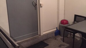 Una habitació amb una porta gris, una taula petita amb una cadira, un escombriaire blau i un safataire vermell.