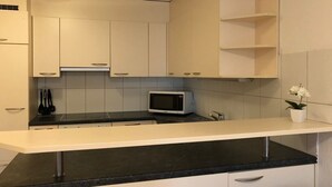 Cuina amb armaris blancs, tauleig negre, microones i una petita planta en test.