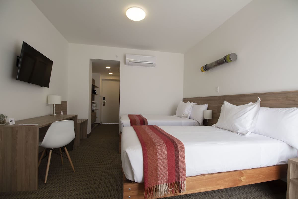 A hotel room with two beds, a desk, a chair, a TV, an air conditioning unit, and a small exercise ball.
